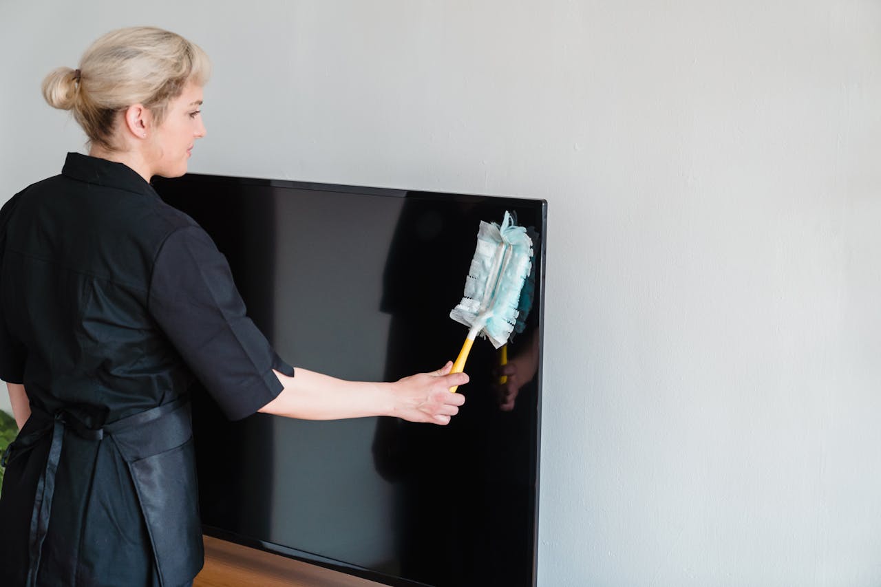 why-choose-us A female housekeeper performing dusting on a television screen indoors.